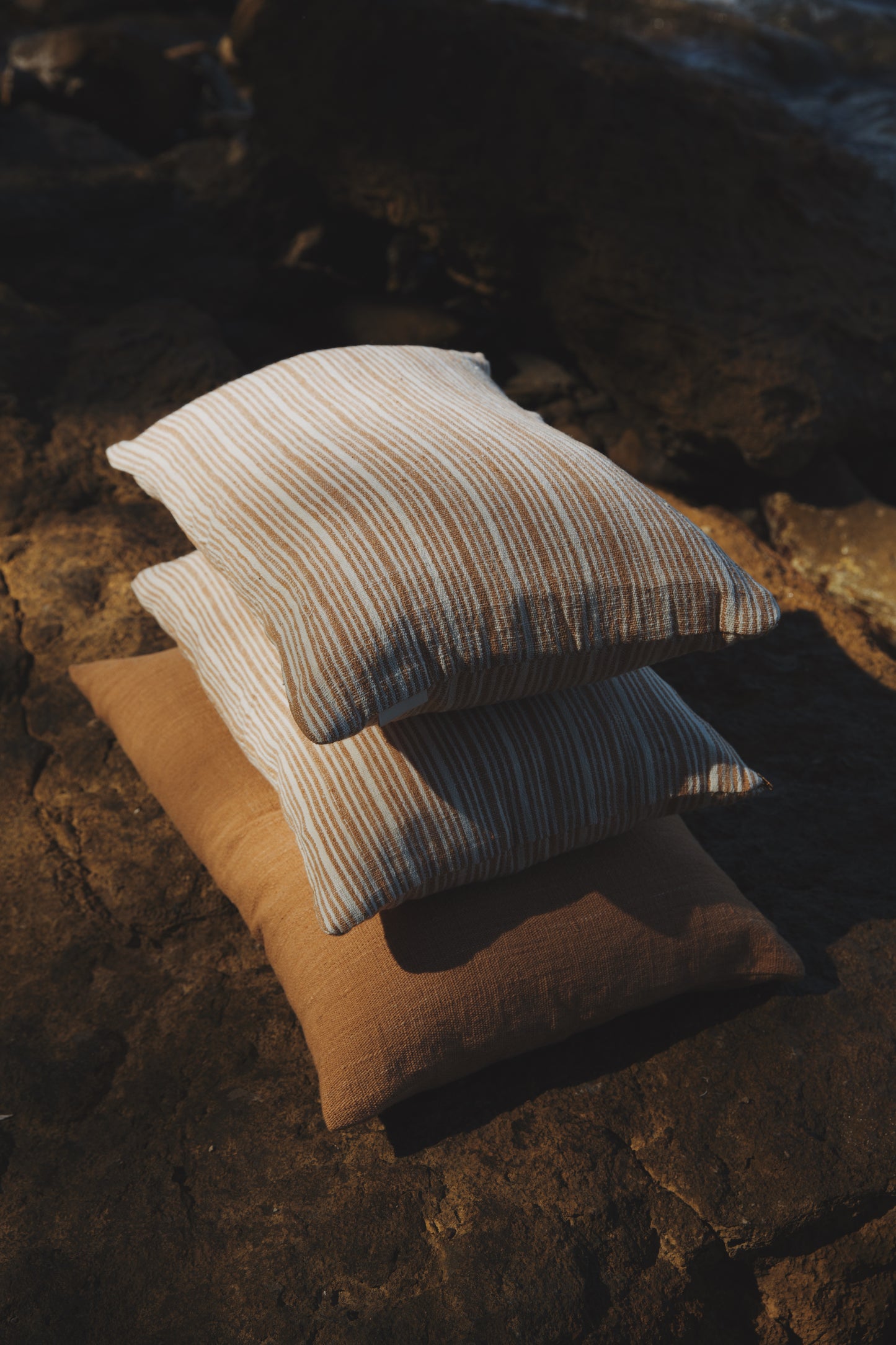 Three pillows stacked on a textured surface with warm lighting