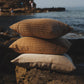 Three pillows stacked on a rock with a scenic background of water and cliffs.