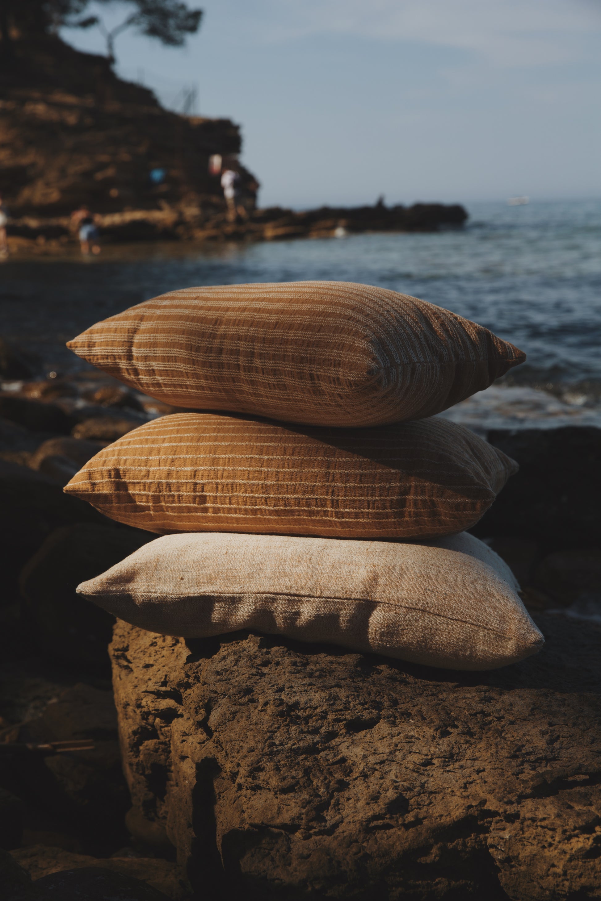 Three pillows stacked on a rock with a scenic background of water and cliffs.