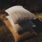 Three pillows stacked on a textured surface with warm lighting