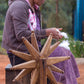 Woman spinning yarn using a wooden spinning wheel outdoors.