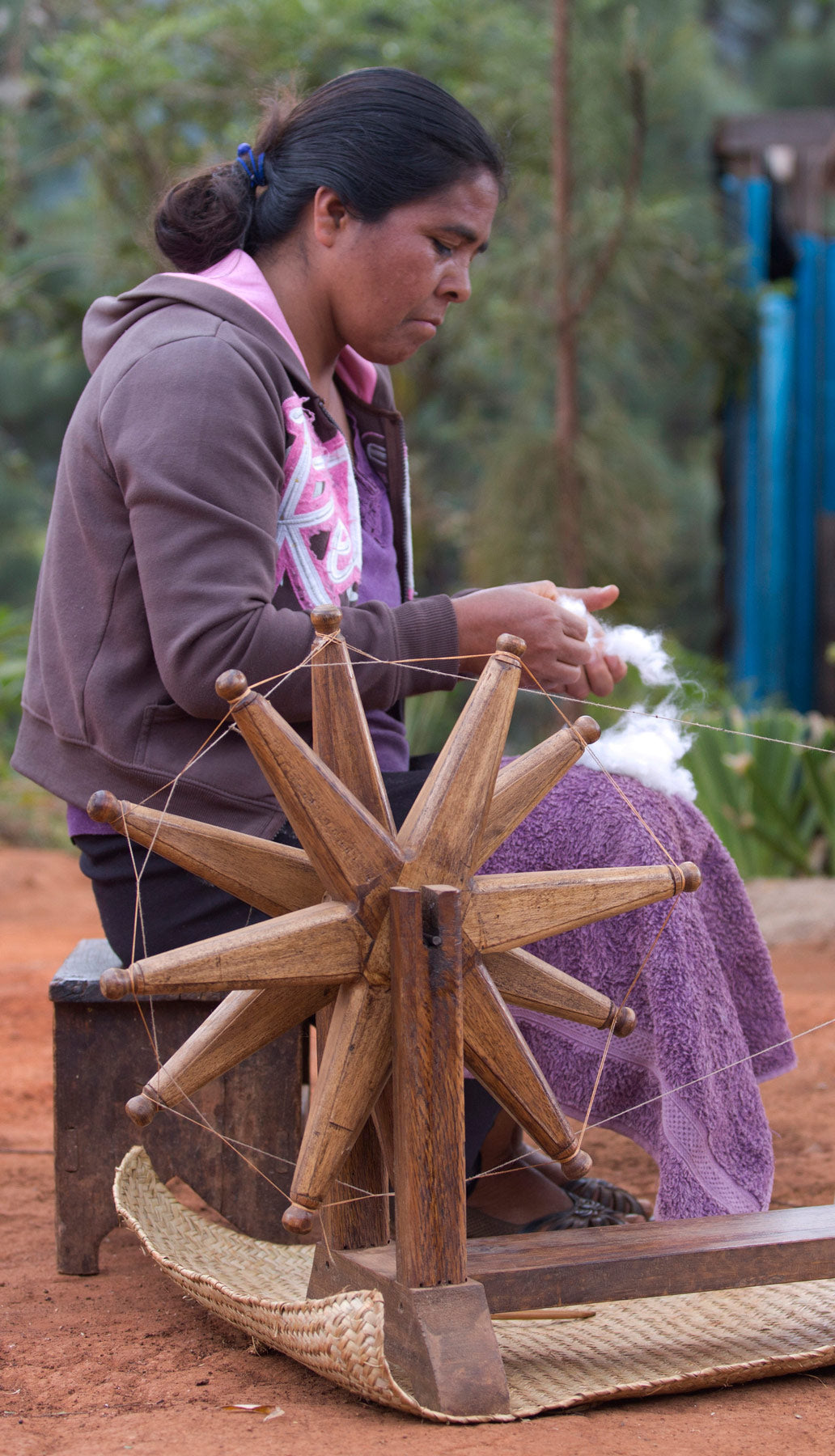 Woman spinning yarn using a wooden spinning wheel outdoors.